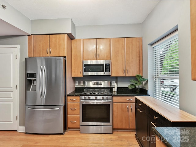 kitchen with appliances with stainless steel finishes, light wood-type flooring, and dark stone countertops