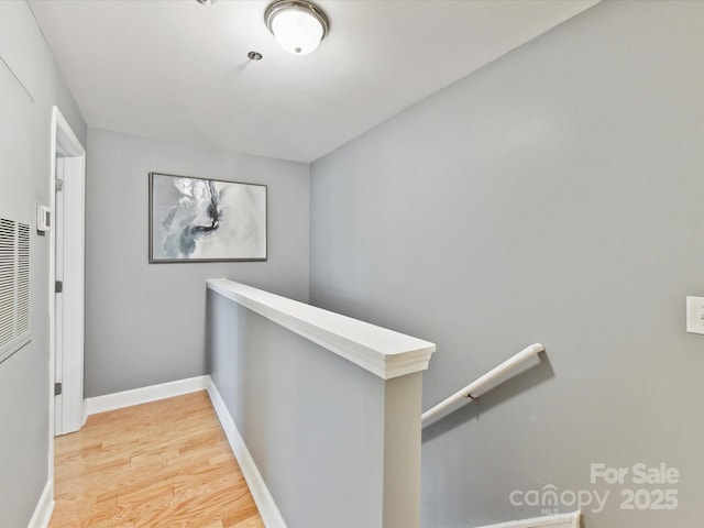 hallway with an upstairs landing, light wood-style floors, and baseboards