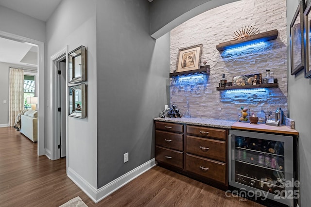 indoor bar with wine cooler, dark wood finished floors, and baseboards
