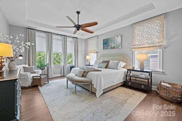 bedroom featuring a tray ceiling, wood finished floors, a ceiling fan, baseboards, and ornamental molding