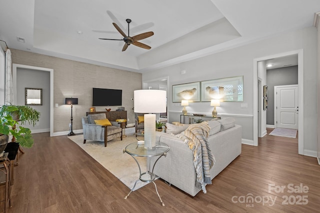 living room with ceiling fan, a raised ceiling, wood finished floors, and baseboards
