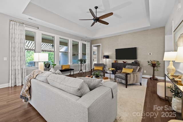 living room with a tray ceiling, baseboards, a ceiling fan, and wood finished floors