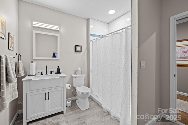 bathroom featuring wood finished floors, vanity, baseboards, toilet, and curtained shower