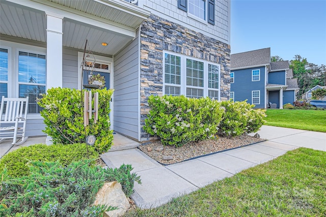 entrance to property featuring stone siding, a lawn, and a porch