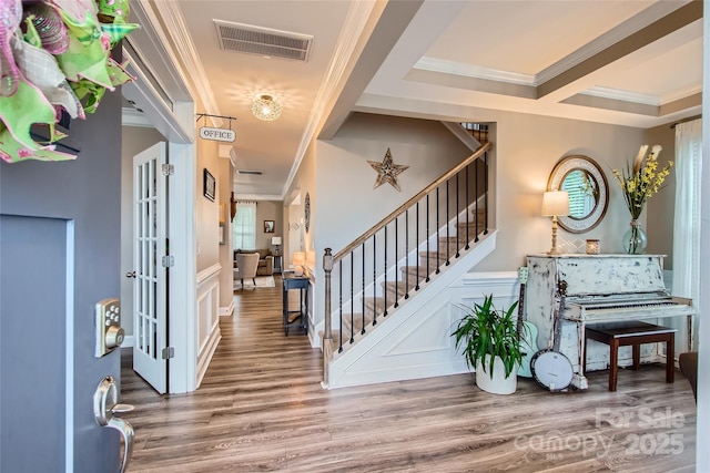 foyer with ornamental molding, wood finished floors, stairs, a decorative wall, and wainscoting