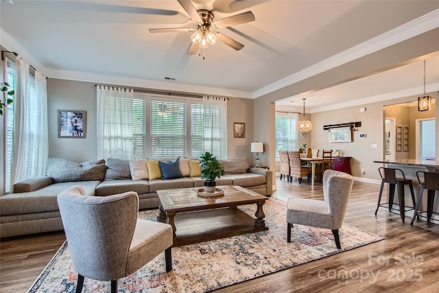 living area featuring plenty of natural light, crown molding, wood finished floors, ceiling fan, and baseboards