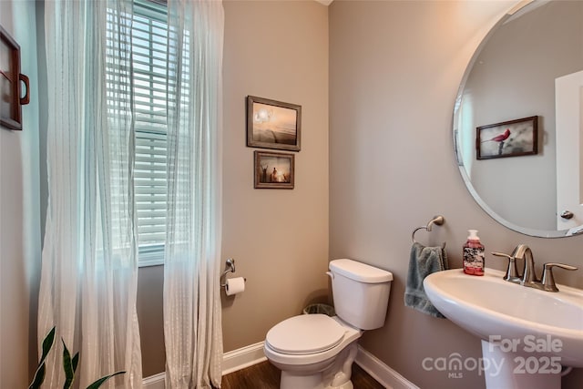 half bathroom with toilet, baseboards, a sink, and wood finished floors