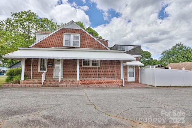 view of front of house with covered porch, fence, and brick siding