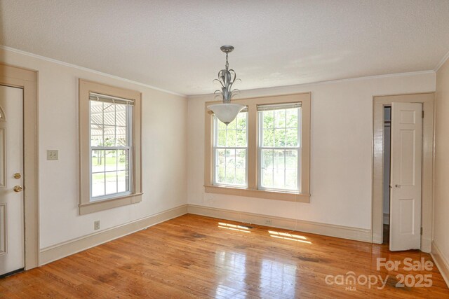 unfurnished dining area with wood finished floors, crown molding, baseboards, and a textured ceiling