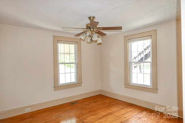 spare room featuring plenty of natural light, a textured ceiling, baseboards, light wood-type flooring, and a ceiling fan