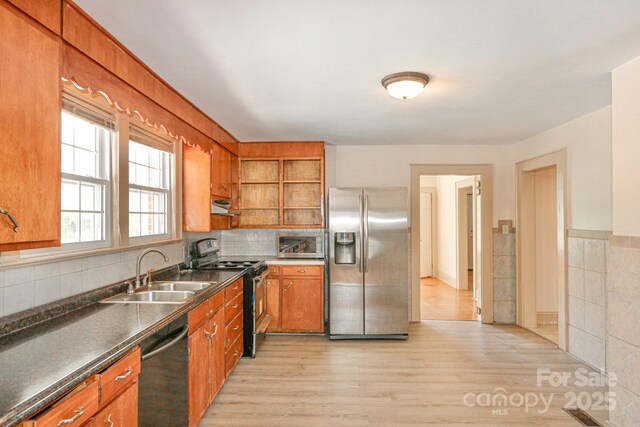 kitchen with appliances with stainless steel finishes, a sink, brown cabinets, dark countertops, and light wood-style floors