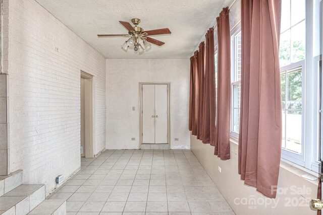spare room featuring ceiling fan, a textured ceiling, brick wall, and light tile patterned floors