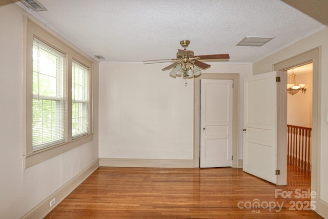 empty room with wood finished floors, crown molding, ceiling fan, a textured ceiling, and a chandelier