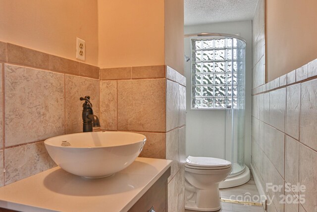 full bathroom featuring tile walls, vanity, toilet, a textured ceiling, and a wainscoted wall