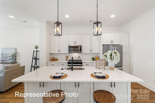 kitchen with appliances with stainless steel finishes, decorative backsplash, white cabinets, a center island with sink, and a kitchen breakfast bar
