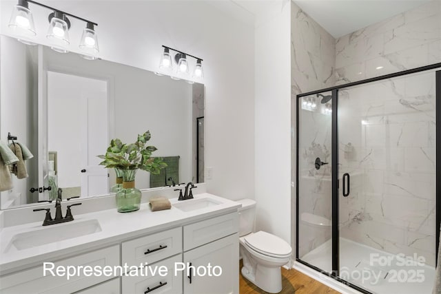 bathroom with toilet, a marble finish shower, double vanity, and wood finished floors