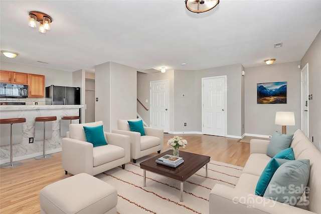 living area with light wood-style flooring, baseboards, and stairway