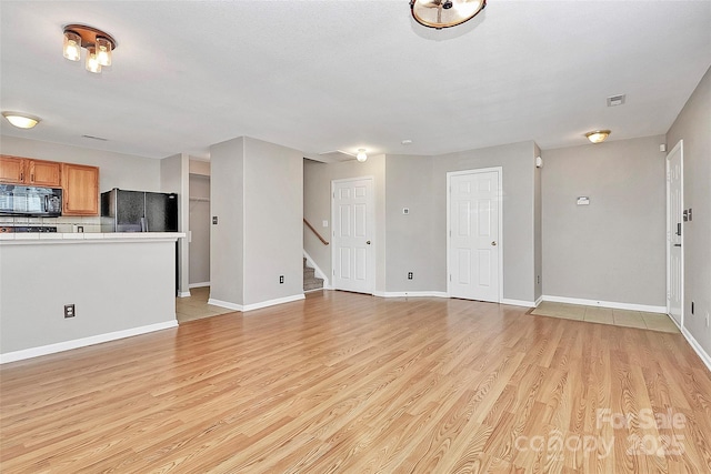 unfurnished living room featuring light wood-style flooring, stairs, and baseboards
