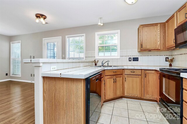 kitchen featuring black appliances, a peninsula, a sink, and decorative backsplash