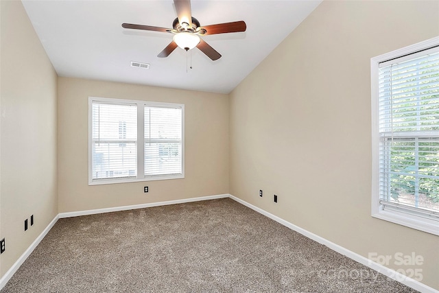 spare room featuring healthy amount of natural light, dark colored carpet, ceiling fan, and baseboards