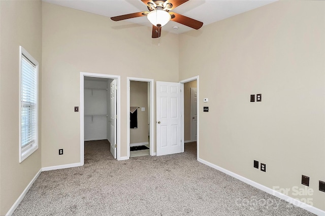 unfurnished bedroom featuring a towering ceiling, carpet floors, baseboards, a walk in closet, and ceiling fan