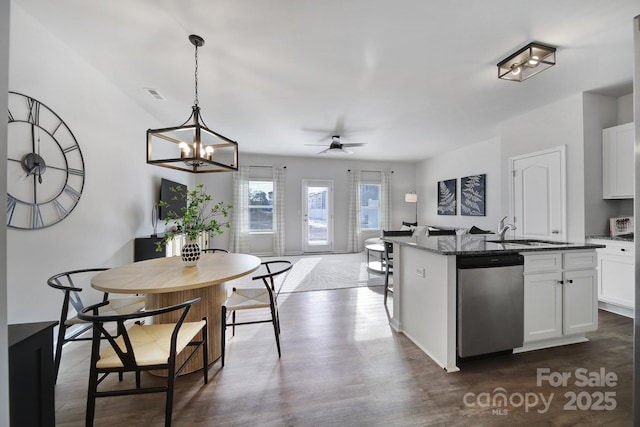 kitchen with stainless steel dishwasher, a sink, dark stone counters, and white cabinetry