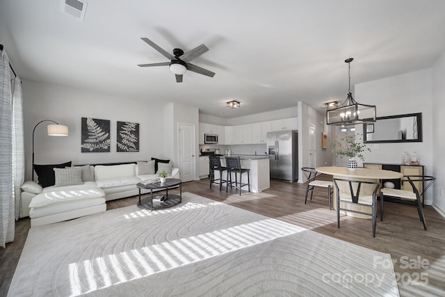 living room with a chandelier, dark wood-style floors, a ceiling fan, and baseboards