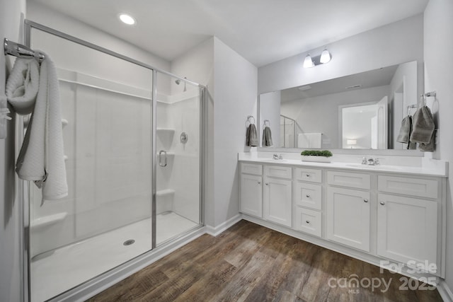 full bathroom featuring a stall shower, double vanity, wood finished floors, baseboards, and recessed lighting