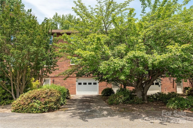 view of property hidden behind natural elements with brick siding, a garage, and driveway