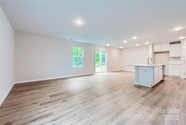 kitchen featuring open floor plan, light wood finished floors, white cabinets, a sink, and recessed lighting