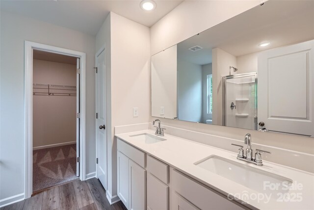 bathroom with a stall shower, wood finished floors, a walk in closet, and double vanity