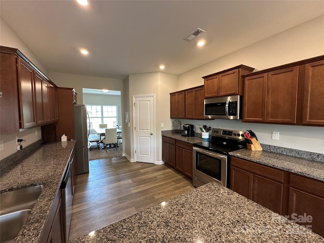 kitchen with stainless steel appliances, a sink, dark wood-type flooring, dark stone countertops, and recessed lighting