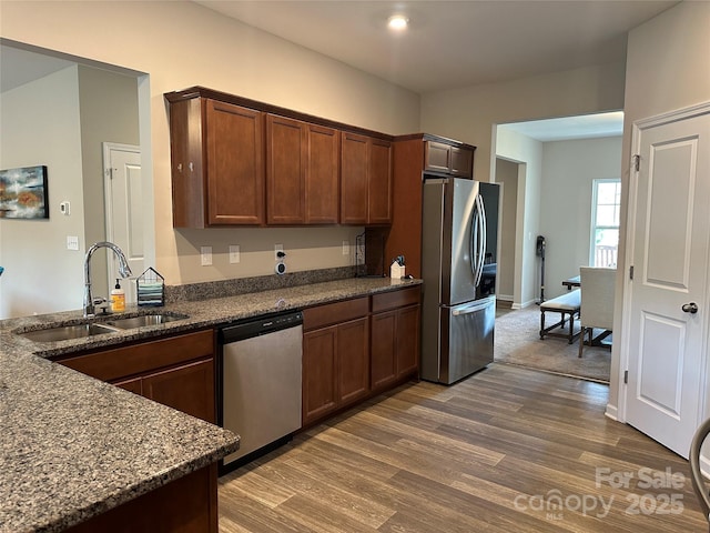 kitchen with stainless steel appliances, a sink, dark wood-type flooring, dark stone counters, and baseboards