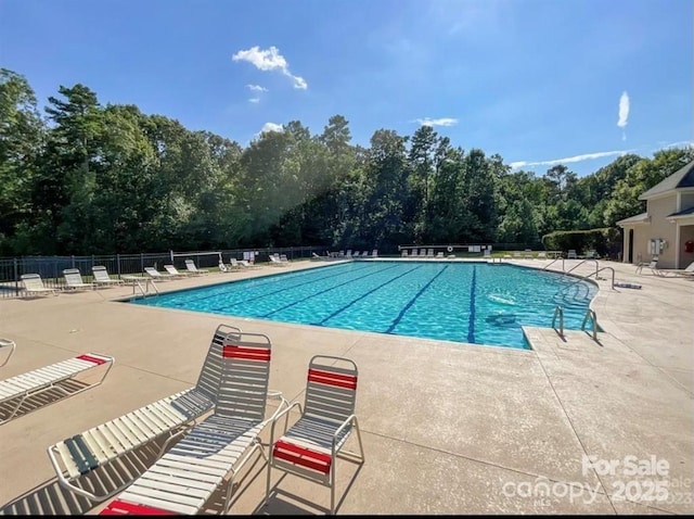 community pool with fence, a patio, and view of scattered trees