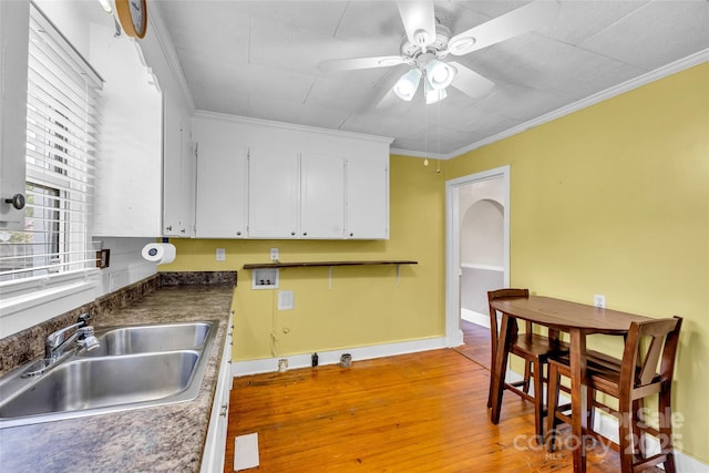 kitchen featuring a sink, a ceiling fan, white cabinets, light wood-style flooring, and ornamental molding
