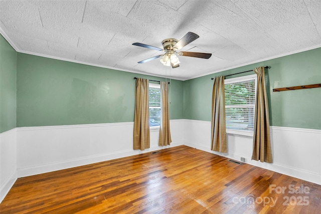 unfurnished room featuring plenty of natural light, hardwood / wood-style flooring, ceiling fan, ornamental molding, and a textured ceiling