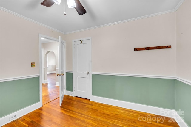 spare room featuring wood finished floors, a ceiling fan, arched walkways, ornamental molding, and baseboards