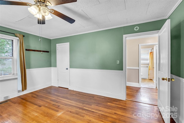 empty room with wood finished floors, a ceiling fan, and crown molding
