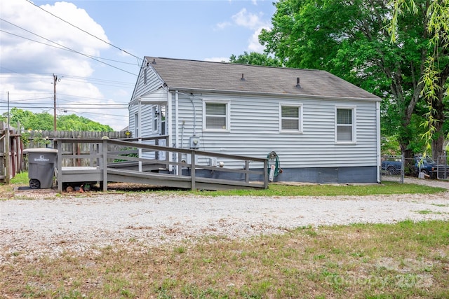 view of home's exterior with fence, a wooden deck, and roof with shingles