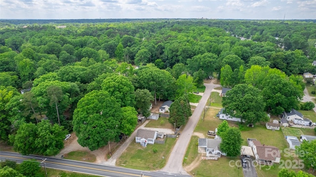 aerial view of property and surrounding area featuring a forest and nearby suburban area
