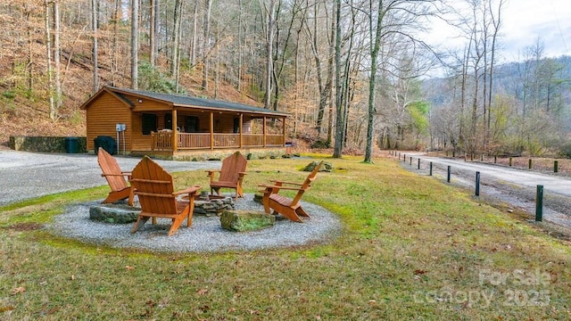 view of jungle gym with a fire pit, covered porch, a yard, and a view of trees