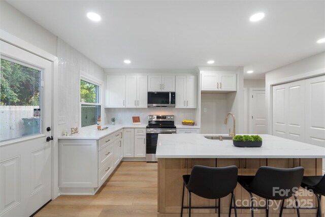 4042 Uppergate Ln, Charlotte, NC 28215 - kitchen with stainless steel appliances, white cabinets, light wood finished floors, recessed lighting, and a kitchen breakfast bar