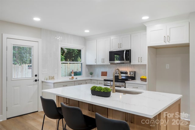4042 Uppergate Ln, Charlotte, NC 28215 - kitchen featuring stainless steel appliances, light wood-type flooring, an island with sink, light stone counters, and decorative backsplash