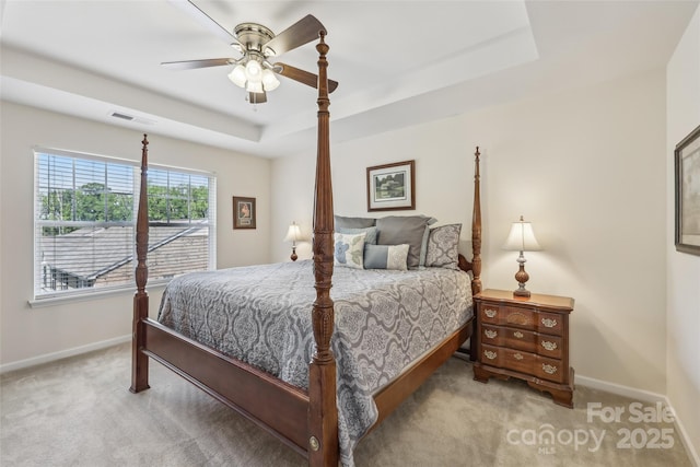 carpeted bedroom with baseboards, a tray ceiling, and ceiling fan