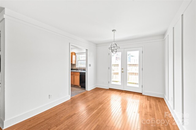 unfurnished dining area with light wood-type flooring, a chandelier, french doors, and baseboards