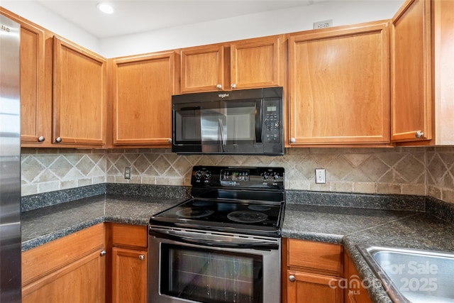 kitchen featuring stainless steel appliances, dark countertops, decorative backsplash, and a sink