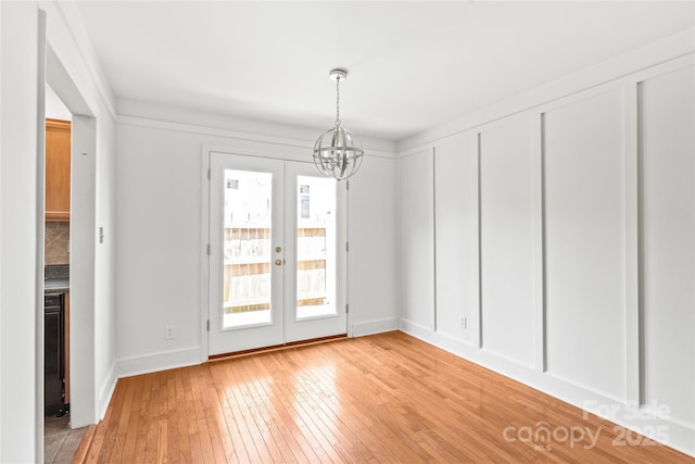 unfurnished dining area featuring light wood-type flooring, a chandelier, french doors, and baseboards