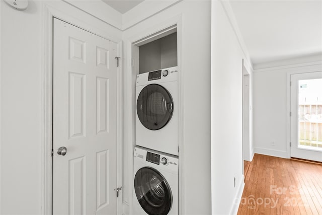 clothes washing area featuring stacked washer / dryer, light wood finished floors, and baseboards