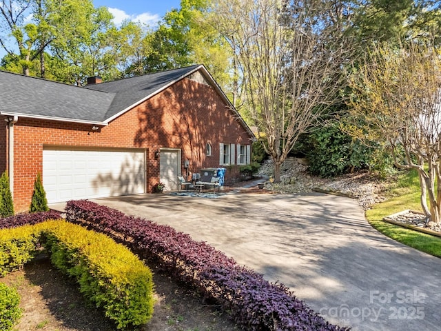 view of property exterior with brick siding, driveway, a garage, a chimney, and roof with shingles