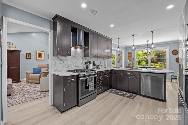 kitchen with stainless steel appliances, a sink, wall chimney range hood, light wood-style flooring, and ornamental molding